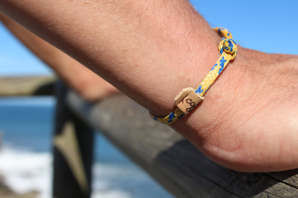Upcycling Armband aus Fischernetz mit Schiebeknoten in Gelb Blau und Detailaufnahme vom Label aus Korkstoff
