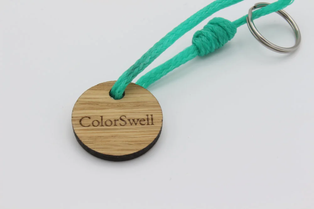 Rückseite der Holzscheibe mit eingelasertem ColorSwell Schriftzug am türkisgrünen Geisternetz Schlüsselanhänger
